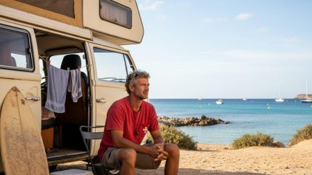 Leben im Wohnmobil: Rettungsschwimmer kämpft mit Wohnkosten auf Mallorca Rettungsschwimmer auf Mallorca steht neben einem Wohnmobil am Strand, symbolisiert Herausforderungen durch hohe Wohnkosten