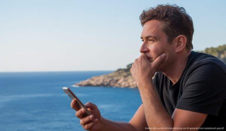 Zwischen Mallorca und Deutschland: Der unerfüllte Traum vom einfachen Leben Eine Person blickt nachdenklich über das Mittelmeer an der Küste von Mallorca, während sie ein Smartphone hält.