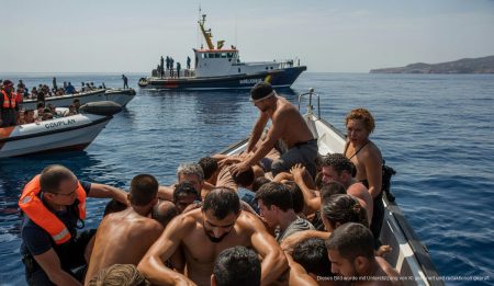 Rettungsoperation im Mittelmeer vor der Küste von Mallorca unter blauem Himmel mit Rettungskräften und Migranten in kleinen Booten.